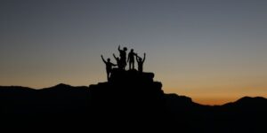 The silhouettes of several people standing on a rock with their hands in the air