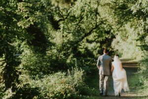 A man and woman in wedding clothes walking down a path in the woods