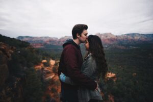 A man kissing the forehead of a woman while standing on a mountain