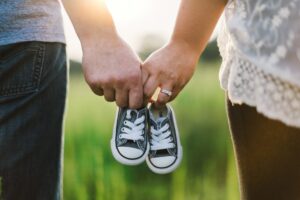 A man and woman holding the same pair of baby shoes