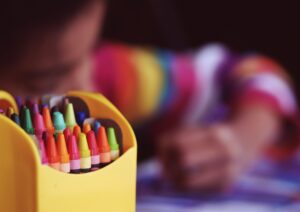a box of crayons with a child coloring in the background