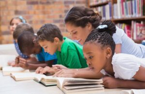 several children and a young woman laying on their stomachs reading books.