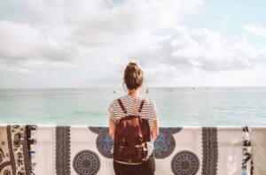 a woman wearing a backpack standing behind a wall looking at the ocean