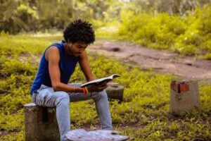 man seated on a rock reading a book