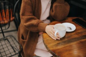 view of a person's body and hand holding a cup of coffee while seated at a round table