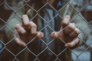 a chain link fence with a  person behind it holding onto the links with their fingers