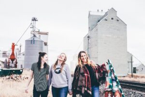 Three women walking near a train track with grain silos behind them