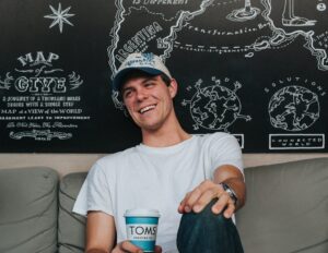 A young man laughing while drinking coffee on a couch