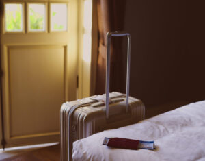 View of a suitcase next to a bed with tickets on it and a door in the background