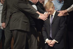 A group of people gathered around a young man praying for him