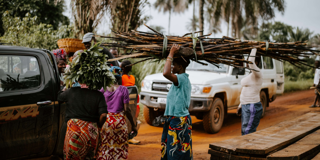 people carrying sticks on their heads down a dirt street