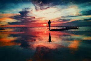 a person standing on a small island surrounded by water holding their arms out looking at the sunset